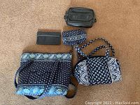 Three bags laid out on beige carpet. Two with Vera Bradley signature fabric patterns in blue tones and one black leather pocket book.