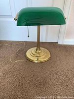 Front view of one green and brass office lamp showing shade, stem, and base.