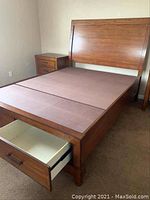 Left side angle of the wooden bed frame showing one open under-bed storage drawer and the left nightstand.