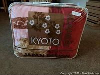 Photo shows packaged Kyoto Raschel blanket in its clear carrying bag with floral design and branding.