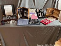 Full view of the tablescape showing the various cutlery sets in wooden cases, the wine opener set, and other items arranged on a gray cloth