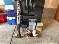 Full lot overview showing upright vacuum cleaner with accessories placed on concrete floor near black fridge