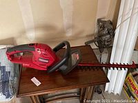 Photo of red Craftsman electric hedge trimmer placed on a wooden table showing entire tool including blade, handles, and body.