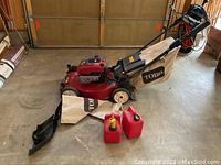 Full lot: Toro mower on concrete floor, grass catcher and chute components removed and laid out, two red gas cans in front