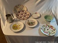 Photo shows the full set of two large dinner plates, four small plates with floral and fruit designs, green bowl, and pewter mug.