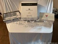 Set of clear wine glasses arranged on white cloth with original packaging boxes behind.