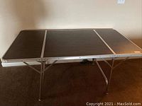 Image showing vintage folding table in standing position with dark wood grain laminate top and metal legs.