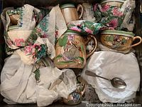 Full view of the antique child's tea set in original box with floral tissue and cloth wrapping showing the teapot, cups, and saucers packed tightly.