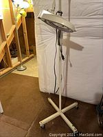 Full view of the rolling magnifying lamp with adjustable arm and caster wheels on a five-legged base.