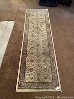 Full view of the rectangular beige rug runner with floral and patterned border placed on carpet.