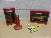 Star Wars Hallmark Christmas ornaments of Queen Amidala and Naboo Starfighter with original boxes displayed on a table against a white brick wall.