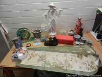 Overall view of assorted Asian decorative items including ceramics, statues, scrolls, and tea cups on a wooden table