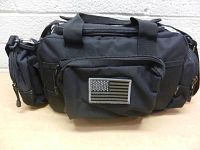Front view of black DBTAC tactical bag showing zippered front pocket with American flag velcro patch and dual handles on top.