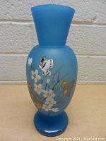 Front view of the matte blue glass vase showing hand painted white flowers and yellow butterflies.