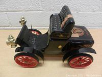 Side profile of the vintage Beam Whiskey decanter in the shape of an early 1900's car, showing brass headlights, black body, red wheels, and gold decals.