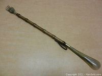 Full view of the back scratcher and shoe horn laid side by side on a beige surface showing their overall length and detailing.