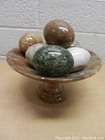 Front and side view of carved marble pedestal dish holding six polished marble decorative eggs in various colors.
