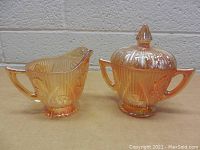 Pair of carnival glass cream and sugar dishes side by side on a wooden surface against a gray wall backdrop
