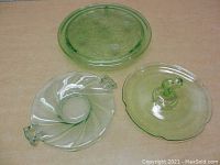 Top down view of three green glass items showing the oval floral serving dish, the twisted swirl platter with handles, and the scalloped edge handled serving tray.