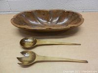 Photo showing the carved wooden salad bowl with matching wooden serving spoon and fork from a side angle on a flat surface.