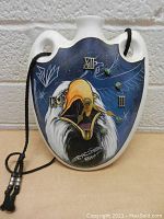 Front view of vintage ceramic pot-shaped clock with painted eagle and Roman numeral clock face, with cord for hanging