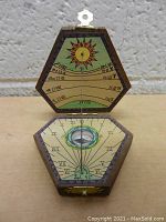 Front view of opened wooden pocket sundial showing sun illustration with zodiac calendar on lid and sundial with compass on base