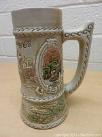 Front and side views of vintage Schlitz Brewing Co. 125th anniversary commemorative beer stein with raised relief brewery scene and decorative handle.