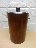 Front view of large vintage wood ice bucket with lid and handle showing wood grain and knob details.