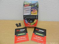 Full view of Scan Gauge II packaging, gauge, quick start guide, user manual, and adhesive pads on wooden surface.