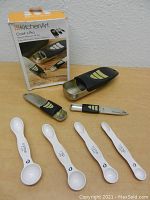 Photo showing KitchenArt Cook's Pro Adjustable Measuring Cups and Spoons displayed with their box and a set of white plastic magnetic measuring spoons.