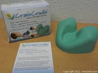 Cranio Cradle device next to its box and instruction flyer showing product details and usage.