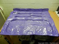 Photo showing multiple large purple zippered storage bags laid flat on a table, with clear plastic compartments on the front.