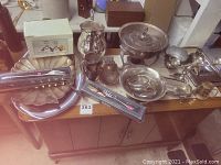 Full view of lot on wooden table showing silver trays, bowls, boxed utensils, trophy cups, pitcher, gravy boat, and weighted sterling candelabra.