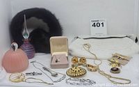 Full lot view showing perfume bottles, vintage Dormar black fur beaded bag, multiple pieces of jewelry including a pendant necklace in a box, bracelets, brooches, and pins arranged on a white surface.
