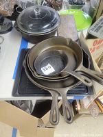 Full view of stacked cast iron frying pans with pot and glass lid in background
