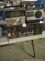Wide angle photo showing the radios stacked on a table, cables visible, and general condition of the radios.