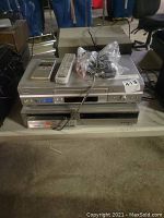 Three stacked Sony video tape players with remote controls and cables on top, showing front panels and controls.