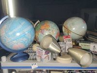 Photo showing three globes, two vintage style and one blue ocean globe, along with a beige dual-lamp mid-century mounted light fixture and assorted small boxes and cards.