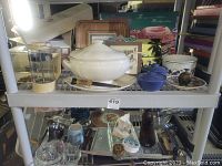 Two shelf view of kitchenware, ceramic, glass, and serving pieces with tureen and blue bowls visible.