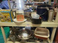 Two shelf display of assorted kitchen items including enamel pots, vintage orange kitchen scale, boxed gelatin set, mixing bowls, metal toaster, and measuring cups.