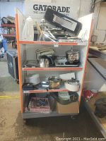 Front view of Gatorade branded metal rolling shelf unit holding various cookware, utensils, and small kitchen appliances stacked across four shelves.