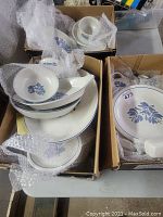 Three boxes of assorted Pfaltzgraff Yorktown dishware wrapped in bubble wrap, showing plates and bowls with blue floral designs