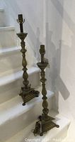 Full view of the pair of electrified candlestick lamps on white stairs, showing overall height and shape.
