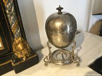Closed view of the silver plated egg coddler with lid and decorative stand.