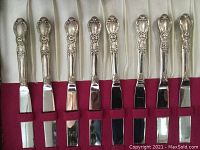 Photo of eight cutting knives with ornate detailed handles, stainless steel blades lying side by side in original box