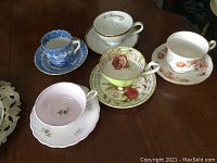 Five varied cups and saucers displayed on a wooden surface showing different floral patterns and designs.