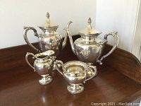Four piece silver plate tea and coffee set including coffee pot, teapot, creamer, and sugar bowl arranged on wooden surface.