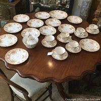 Full view of all dishes spread on wooden table showing 6 cups with saucers, 6 dinner plates, 8 luncheon plates, sugar bowl and creamer.