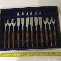 Photo showing full set of six knives and six forks with teak handles in original box with blue velvet lining and white exterior box, measuring about 14 by 10 inches.