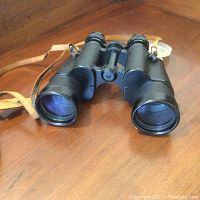 Black Otto Fischer binoculars with neck strap placed on wooden surface.